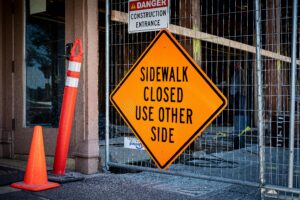 Home 12 Bright orange warning sign indicating sidewalk closure at construction entrance on a temporary fence rental