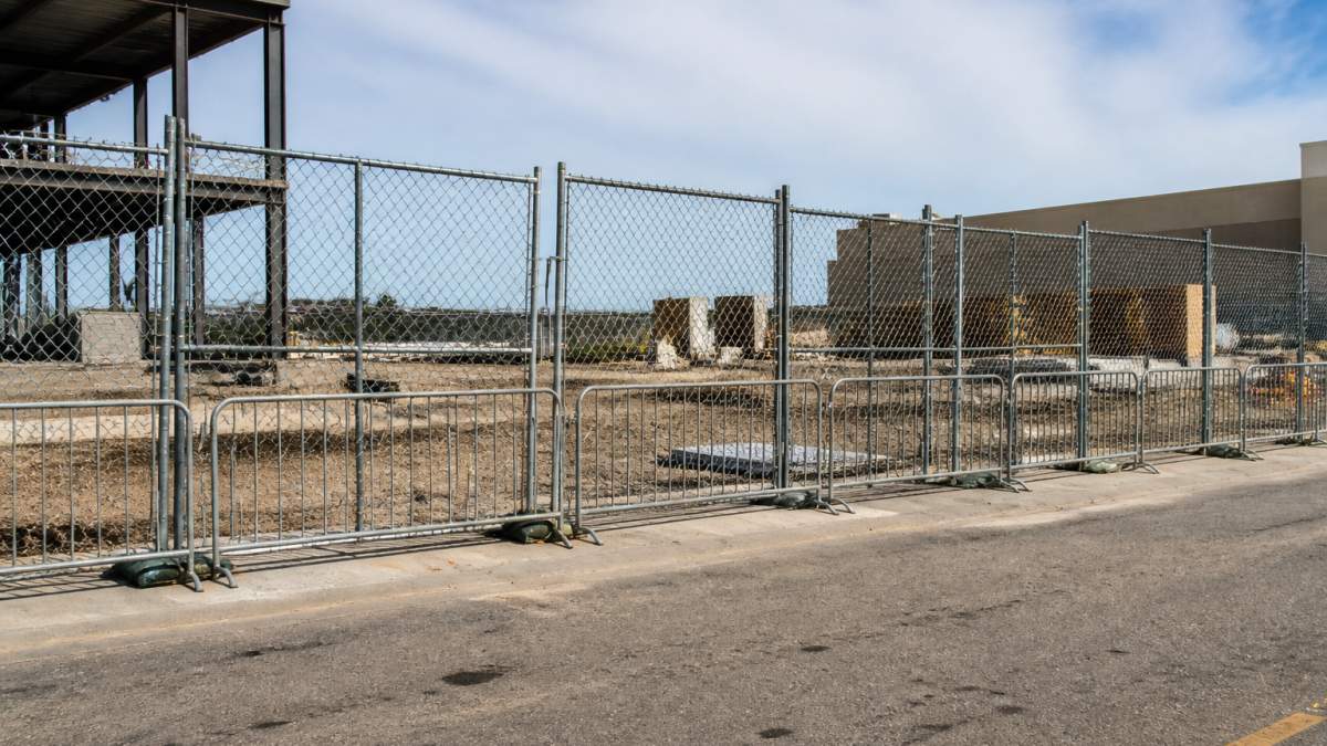 Temporary Fence Rental for Commercial Projects: A 2026 Guide 1 Wide shot of a commercial construction site perimeter secured with chain-link temporary fence panels and steel barricades, showing multiple panel heights and gates
